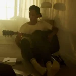 Creator sitting inside a softly lit apartment with calm editorial atmosphere