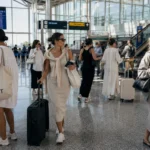 Women wearing relaxed influencer-style dresses while moving through a bright international airport terminal with luggage and casual travel styling.