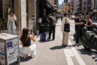 Creators filming fashion and lifestyle content across a busy city street using phones and tripods during daytime.