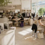 Bright fashion concept store with café seating, creative visitors, natural sunlight, and subtle violet accents in a modern editorial environment.
