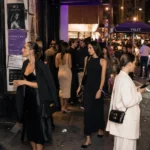 Fashionable guests arriving at a modern evening event wearing relaxed influencer-style dresses outside a busy urban venue.