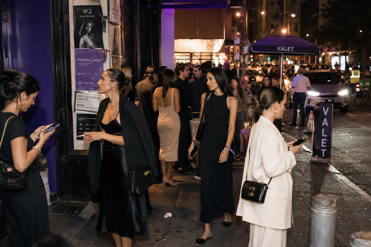 Fashionable guests arriving at a modern evening event wearing relaxed influencer-style dresses outside a busy urban venue.