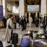 Fashion industry guests inside a luxury hotel lobby during event week with garment bags, stylish luggage, and bright editorial atmosphere.