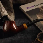 Editorial menswear flat lay featuring a tobacco pipe, textured blazer, luxury watch, and WearDecoded magazine on dark fabric with warm cinematic lighting.