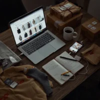 Laptop with online fashion shopping tabs, opened clothing packages, receipts, and folded apparel on a realistic indoor workspace during a sale event.